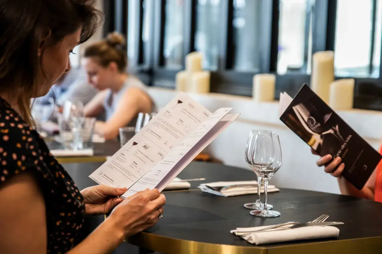Une femme lit la carte des vins, choisissant la quantité de vin parfaite pour son repas.