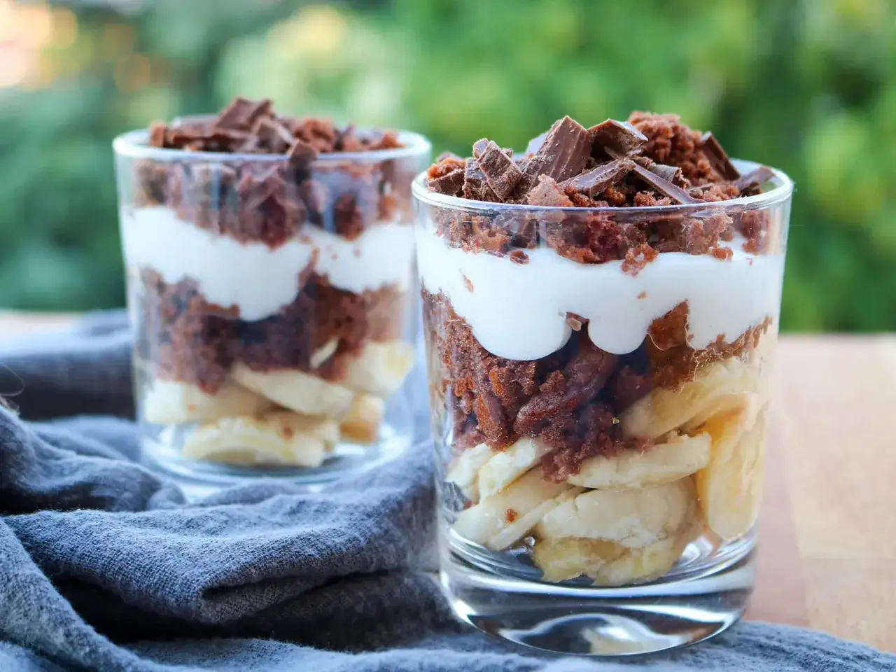 Zwei Gläser mit Schichten aus Bananenscheiben, Schokoladenkuchenstücken und Sahne. Perfekt, um Kuchenreste verwerten!