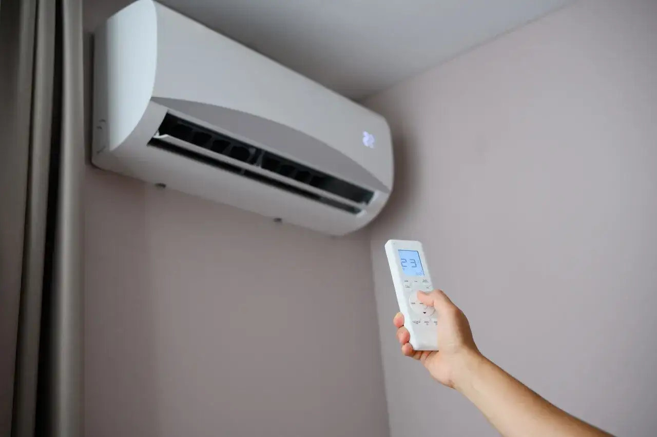 Mano con control remoto ajustando el aire acondicionado, creando una agradable corriente de aire.