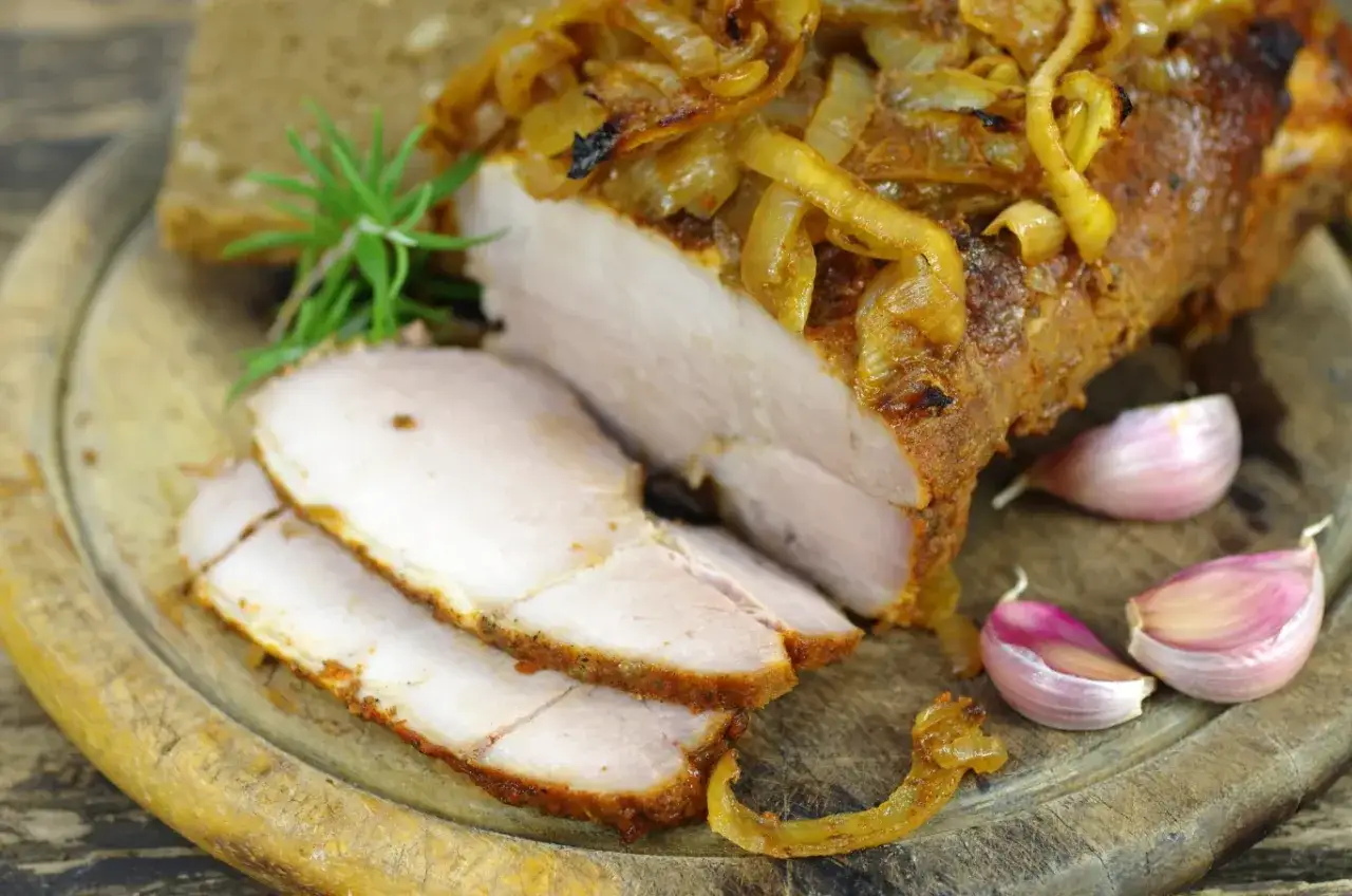 Soczysty schab w mleku, pieczony z cebulką i czosnkiem, podany na desce z chlebem.