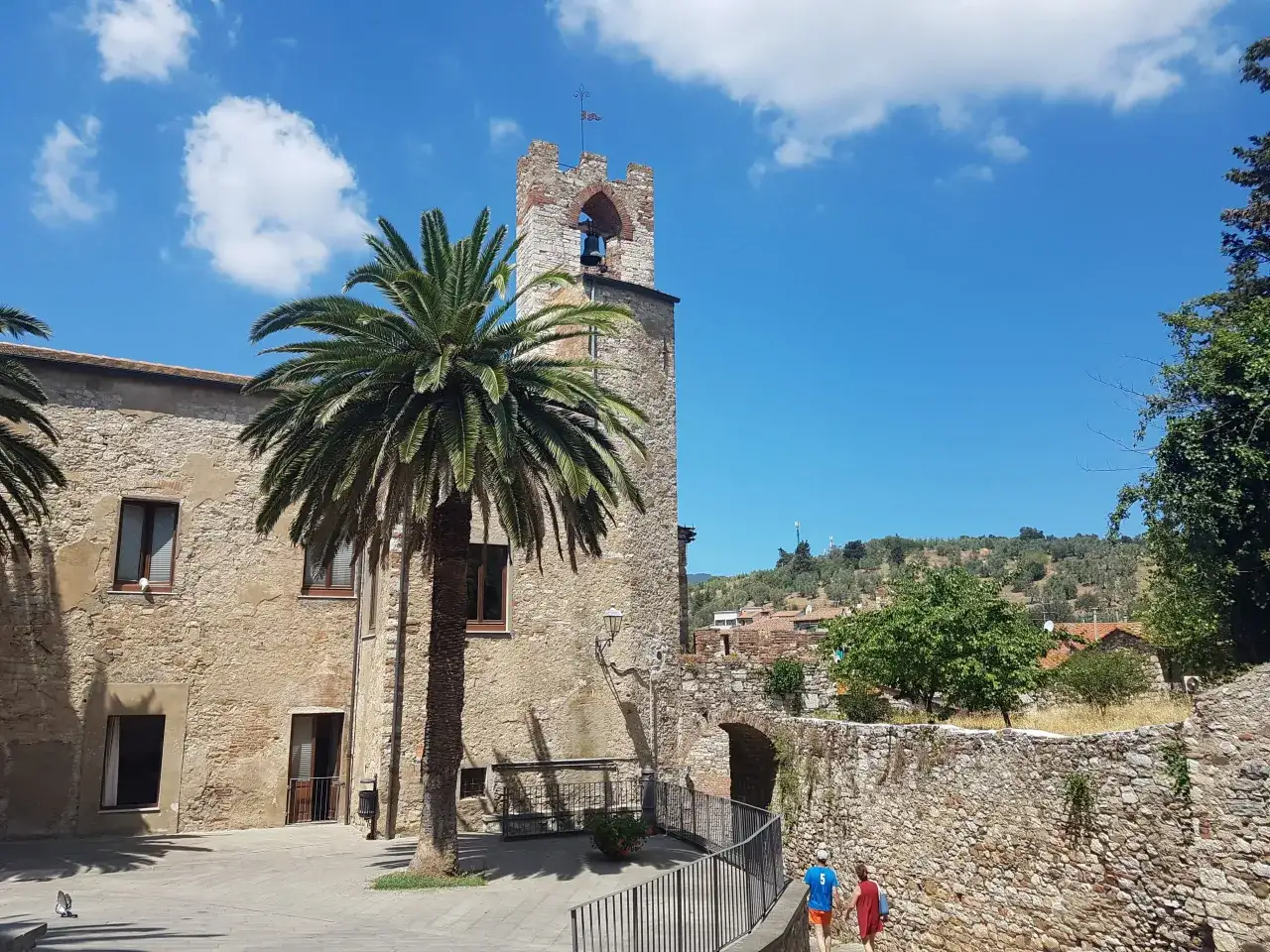 Suvereto, dove si trova questo borgo medievale con torre campanaria, palme e un cielo azzurro.