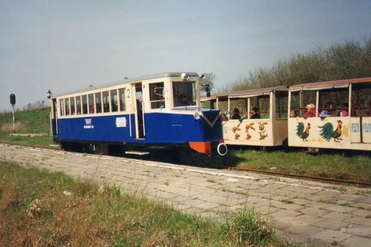 Niebiesko-kremowy szynobus z numerem 2 na bocznym panelu, obok wagonów ozdobionych malunkami zwierząt, czeka na pasażerów.