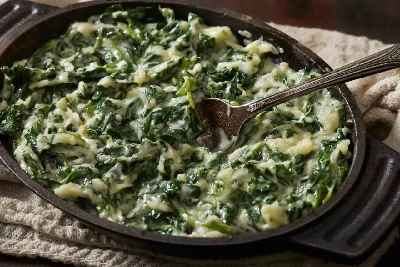 Cremosas espinacas a la crema, servidas en una sart&eacute;n de hierro fundido con una cuchara lista para servir.