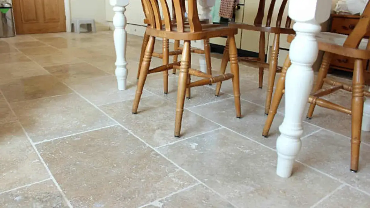 Sol en carrelage poreux beige, avec des pieds de chaises en bois et un pied de table blanc.
