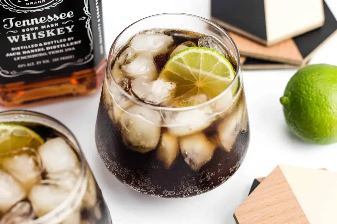 Orzeźwiający jack and coke z lodem i plasterkiem limonki, obok butelka Tennessee Whiskey.