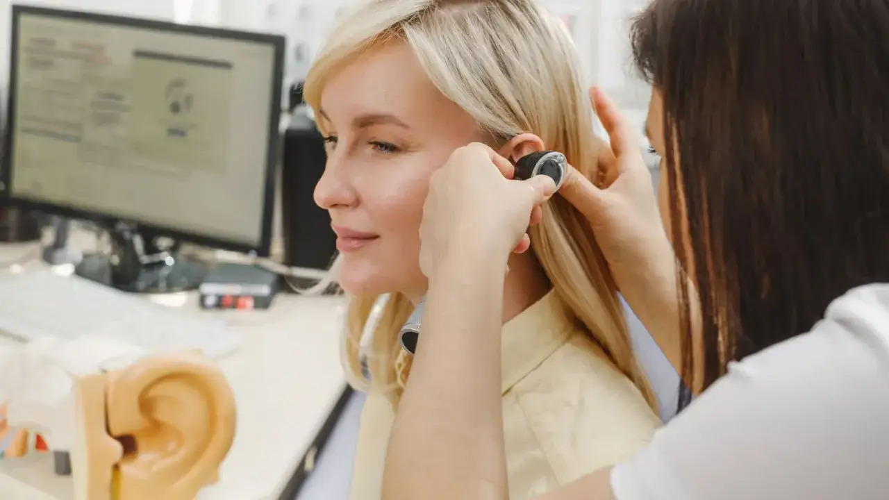 Une audioprothésiste ajuste un appareil auditif. Une formation audioprothésiste à distance est possible pour apprendre ce métier.