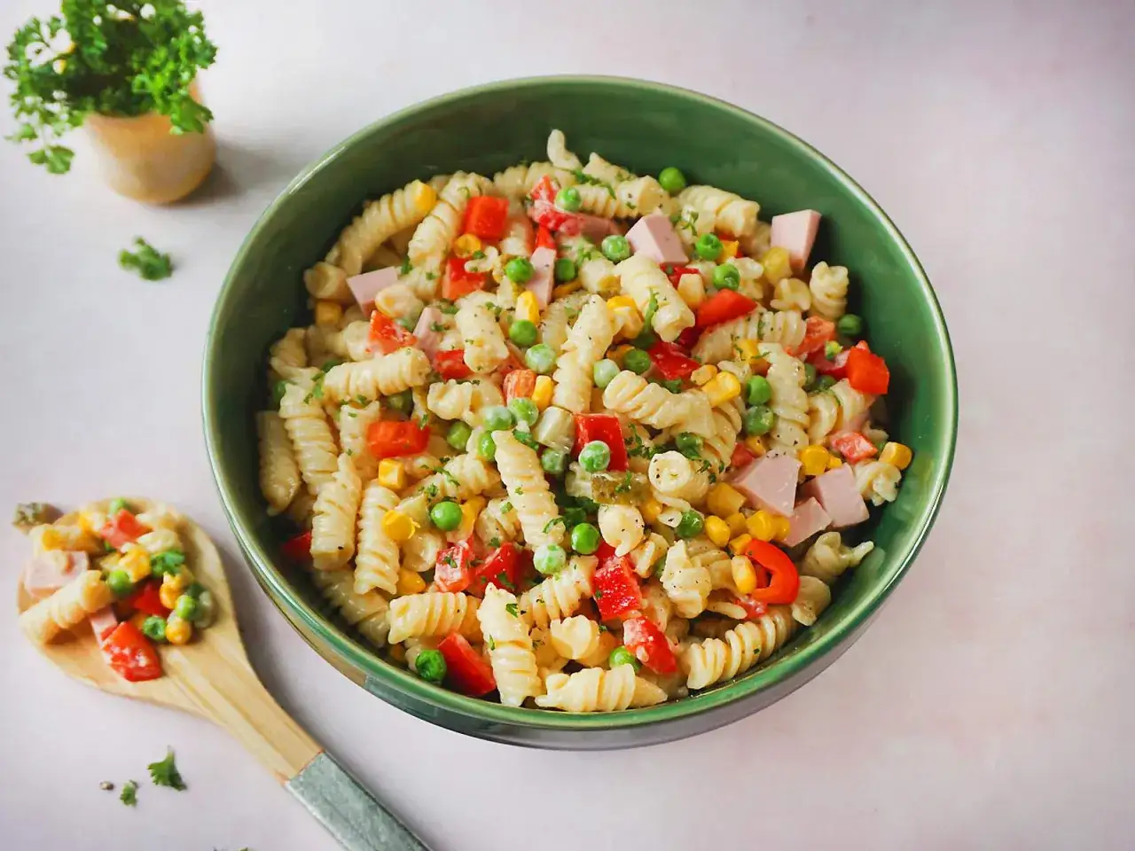 Ein bunter, schneller Nudelsalat mit Spiralnudeln, Erbsen, Mais, Paprika und Schinkenwürfeln in einer grünen Schüssel.