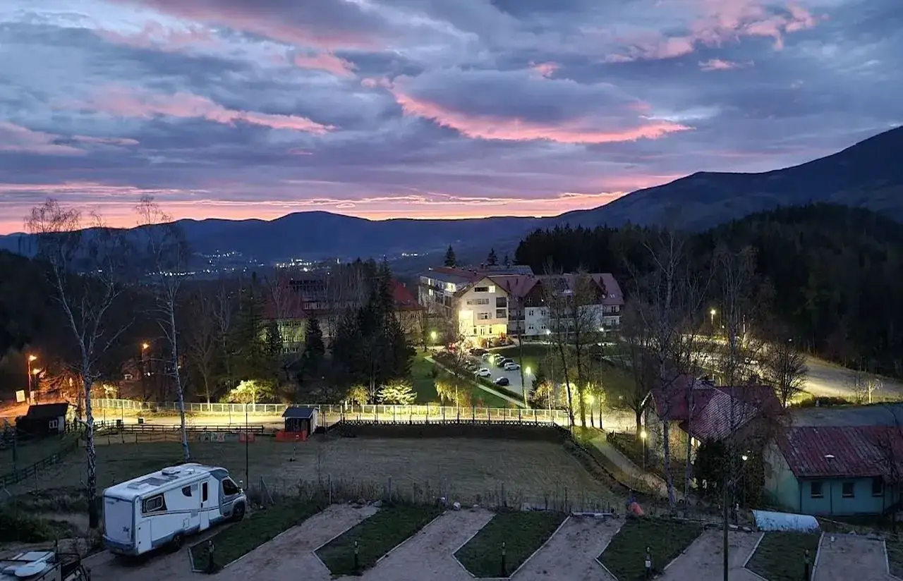 Zachód słońca nad kempingiem Karpacz. Widok na góry, budynki i kampera.