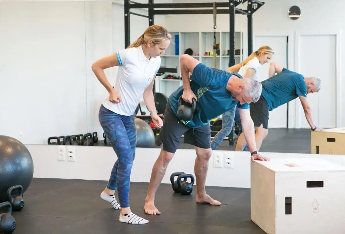 Fizjoterapeutka instruuje mężczyznę wykonującego ćwiczenia z kettlebell. To pokazuje, co jest dobre na zwyrodnienie kręgosłupa: aktywność i rehabilitacja.