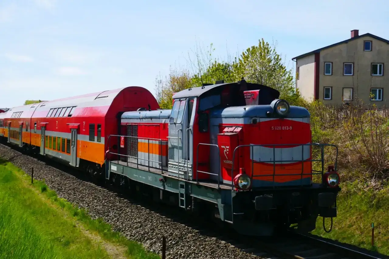 Pociąg SKM Gdynia Hel z czerwono-pomarańczowymi wagonami i lokomotywą SU42-52 jedzie po torach.