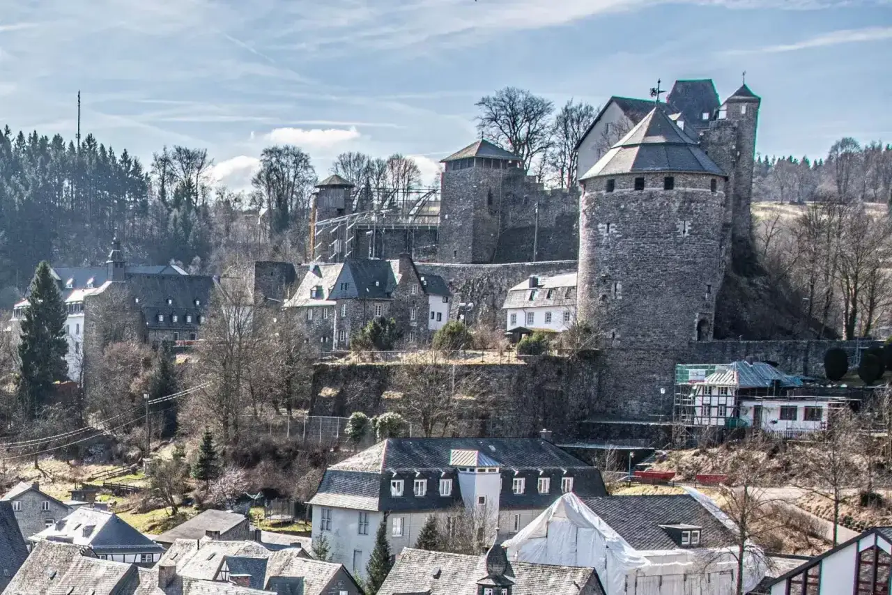 Die Burg Monschau thront über malerischen Fachwerkhäusern. Ein imposanter Bergfried und Wehrmauern dominieren die Szenerie.