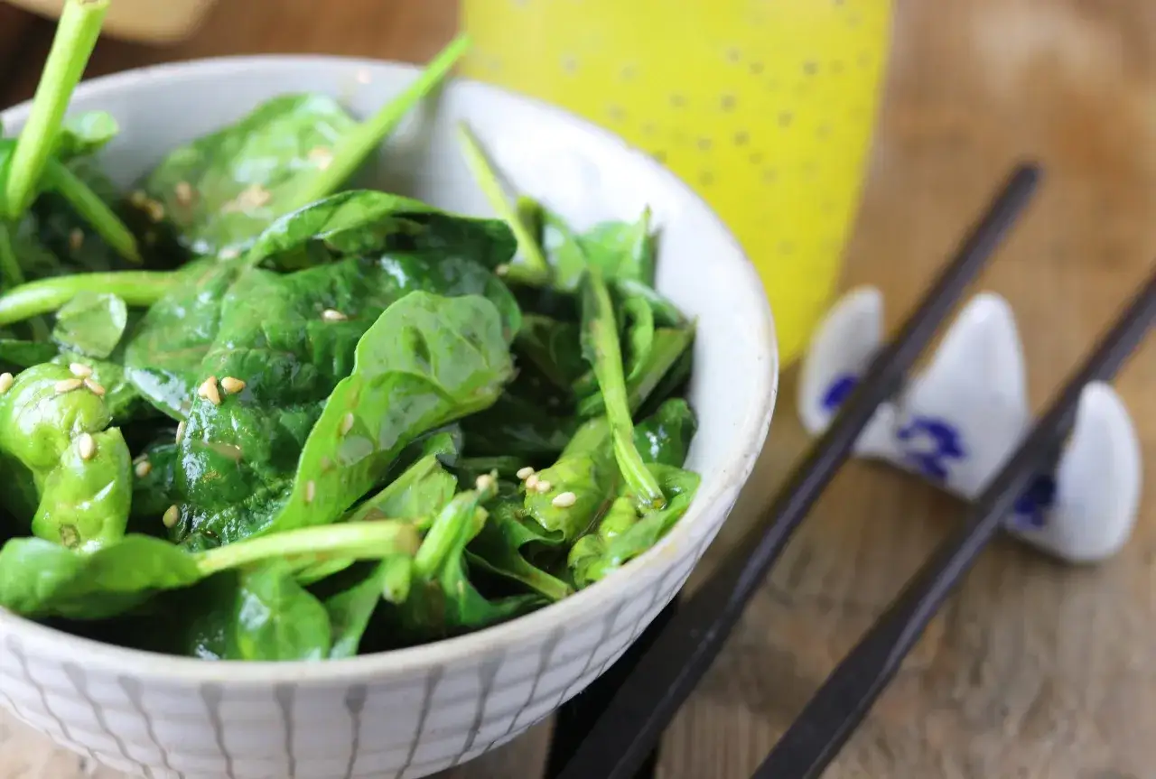 A bowl of glistening spinach gomae, sprinkled with sesame seeds, sits ready to be enjoyed with chopsticks.