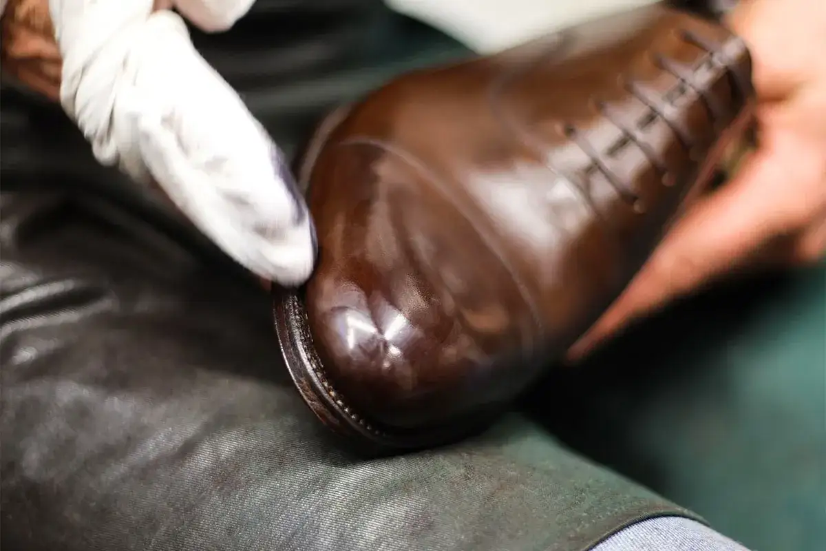 Application de graisse pour chaussures en cuir sur un richelieu marron pour un entretien impeccable.