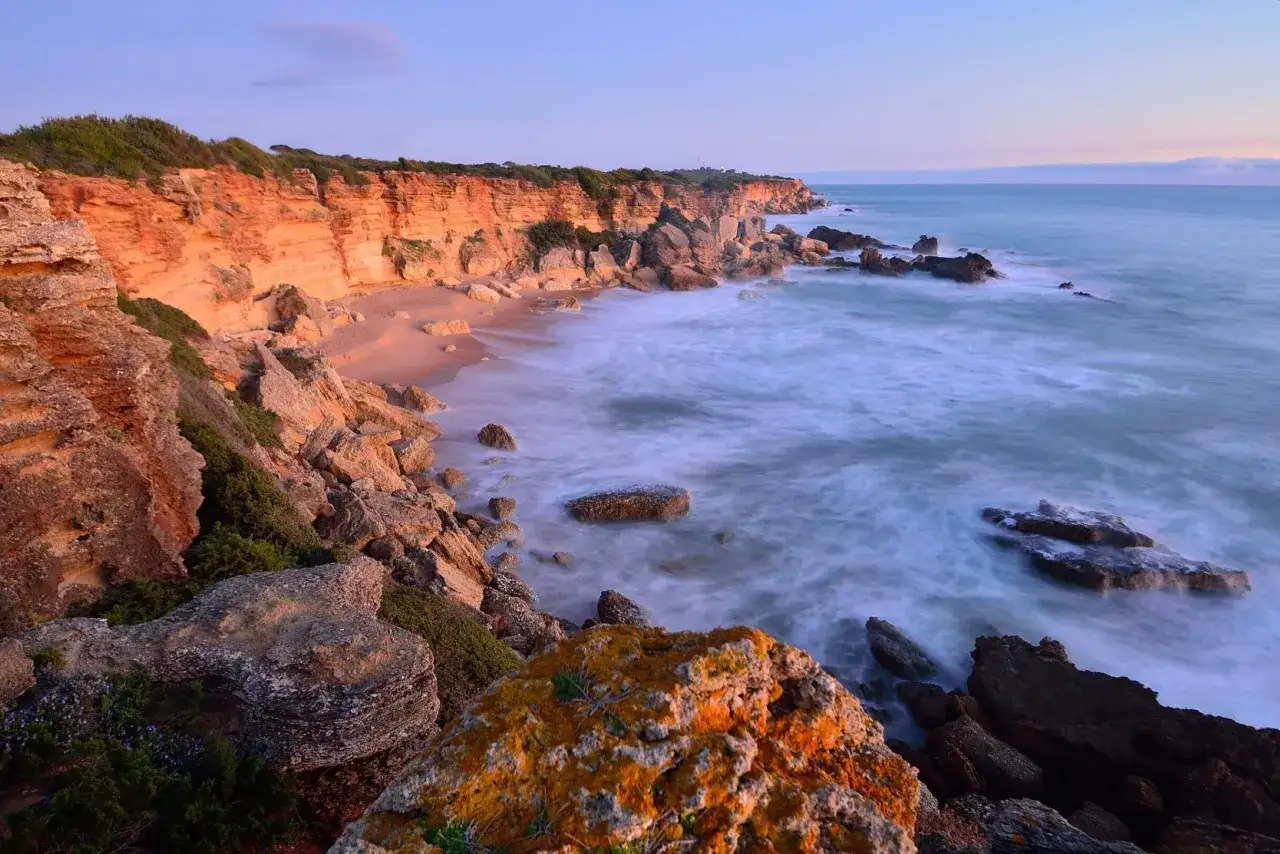 Acantilados anaranjados y mar azul con olas suaves. Un lugar idílico que ver en Conil, perfecto para pasear y disfrutar de la naturaleza.