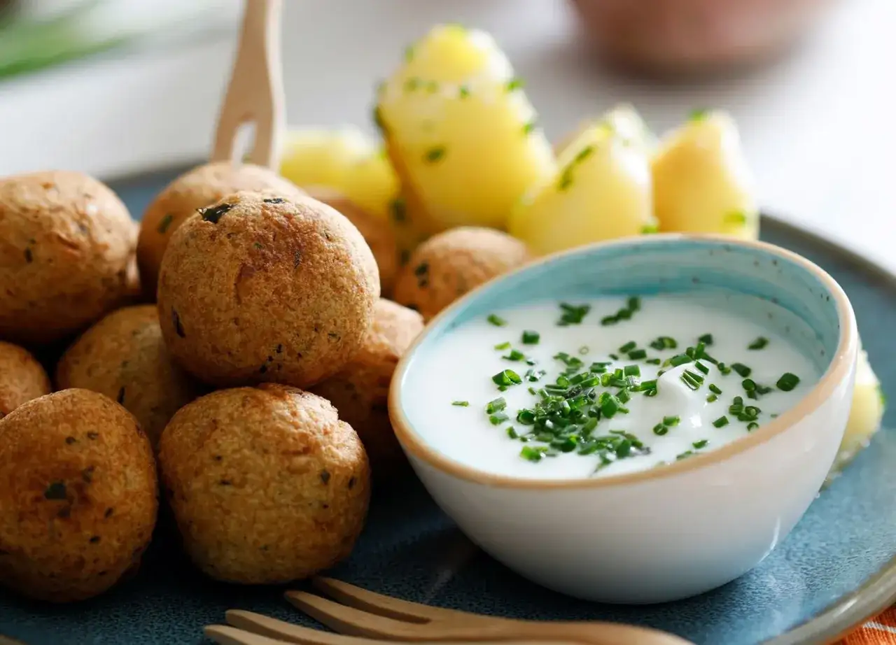Polpette di ceci dorate e croccanti, servite con patate novelle e una ciotola di salsa cremosa guarnita con erba cipollina.