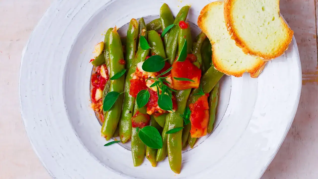 Taccole cosa sono? Ecco un piatto gustoso con taccole verdi cotte in umido con pomodoro e basilico, accompagnate da fette di pane tostato.