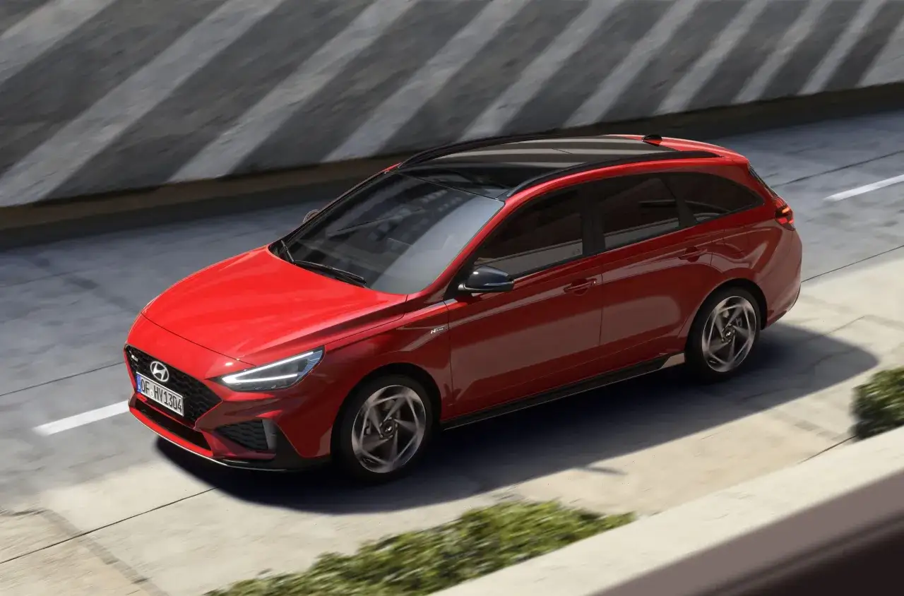 Czerwony Hyundai i30 wagon z czarnym dachem pędzi po drodze, otoczony betonowymi ścianami i zielenią.
