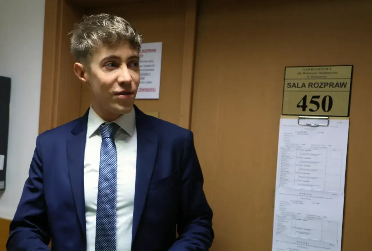 Młody mężczyzna w garniturze przed salą rozpraw 450. Czy najmłodszy polski milioner rzeczywiście zaczął od zera bez pomocy rodziców?