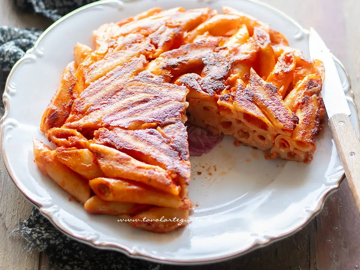 Una deliziosa frittata di pasta, dorata e croccante, servita su un piatto bianco con un coltello.