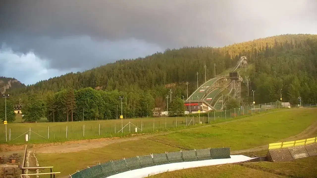 Wielka krokiew trasa skoczni narciarskiej w otoczeniu lasu, pod burzowym niebem.