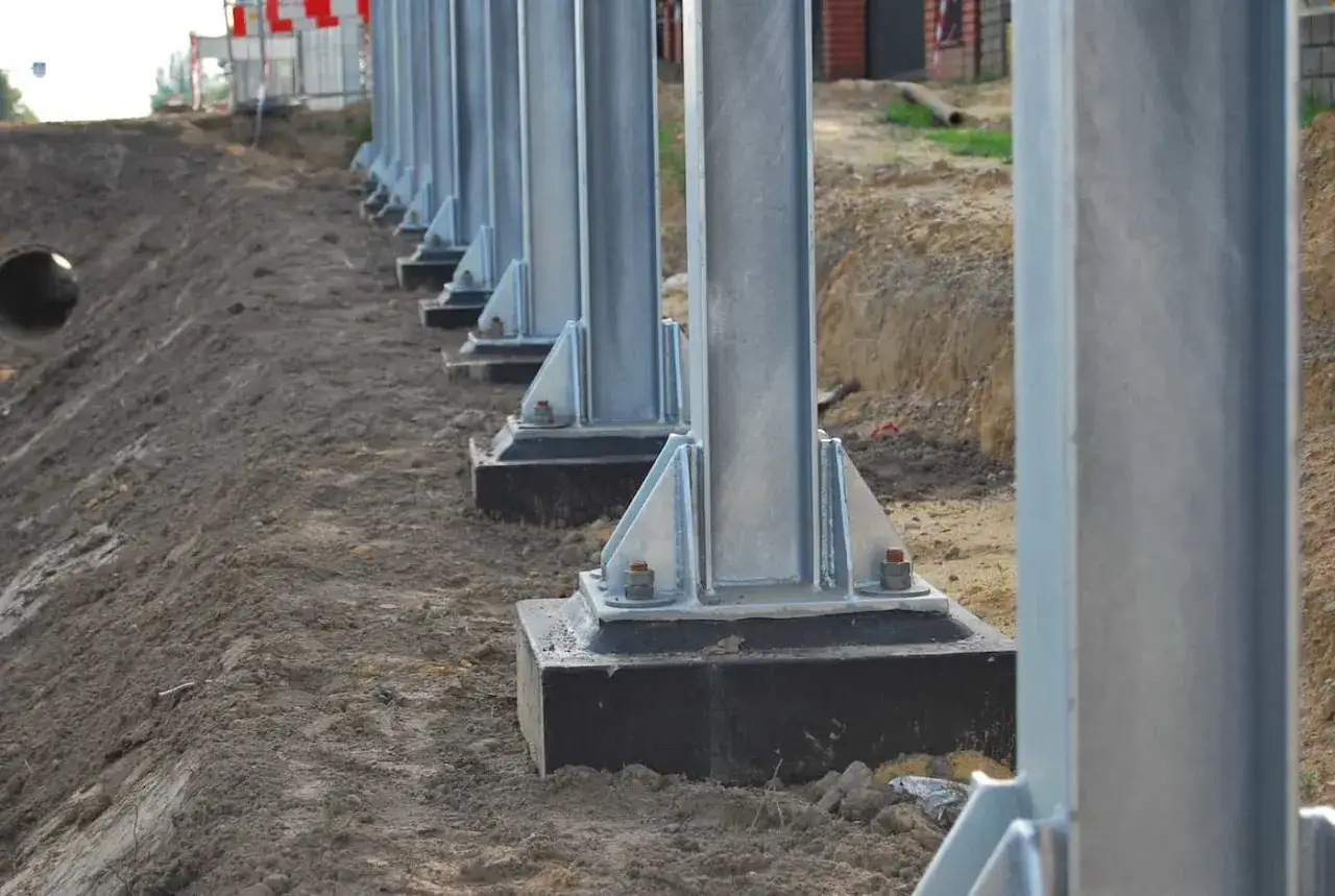 Solidne kotwienie słupów stalowych na budowie. Metalowe słupy osadzone na betonowych podstawach, gotowe do dalszych prac.