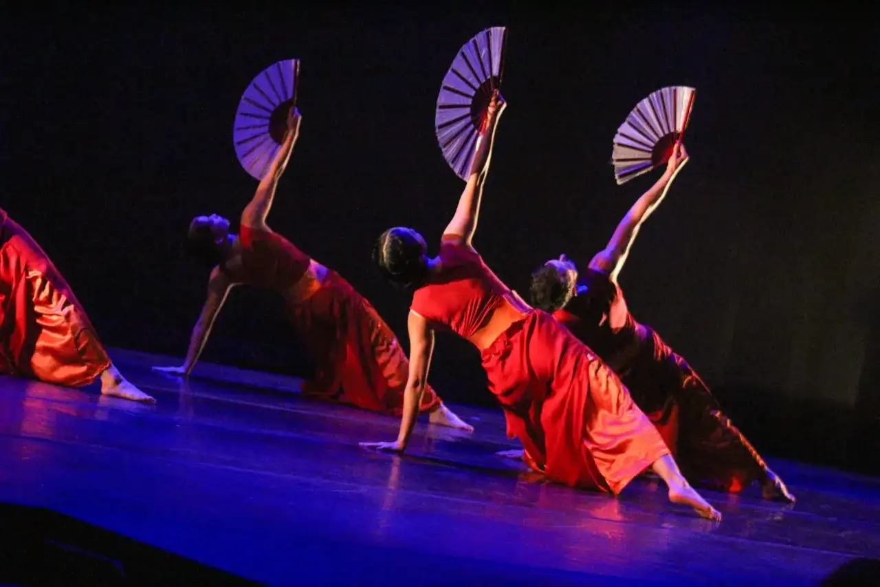 Dancers in red, flowing costumes perform with fans, evoking a story of jordan jutes.