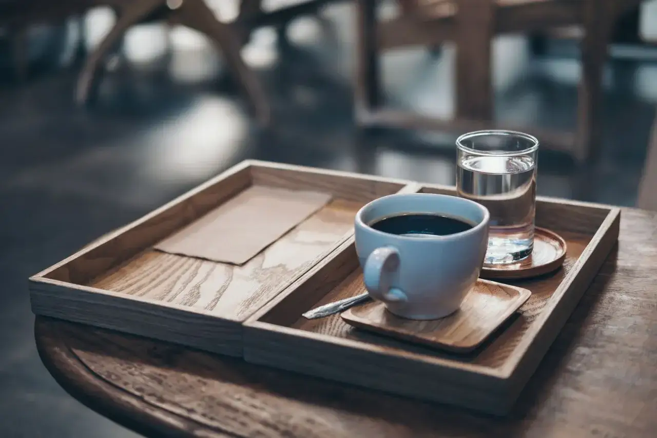 Eine Tasse heißer Kaffee mit einem Glas Wasser auf einem Holzteller.