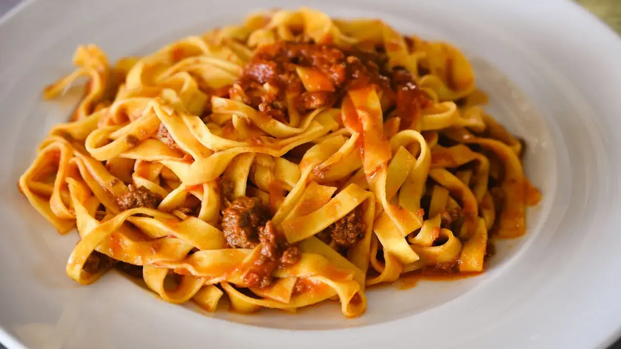 Tagliatelle al rag&ugrave;, un classico piatto servito in un'osteria a Bologna, invitano a un viaggio di sapori autentici.