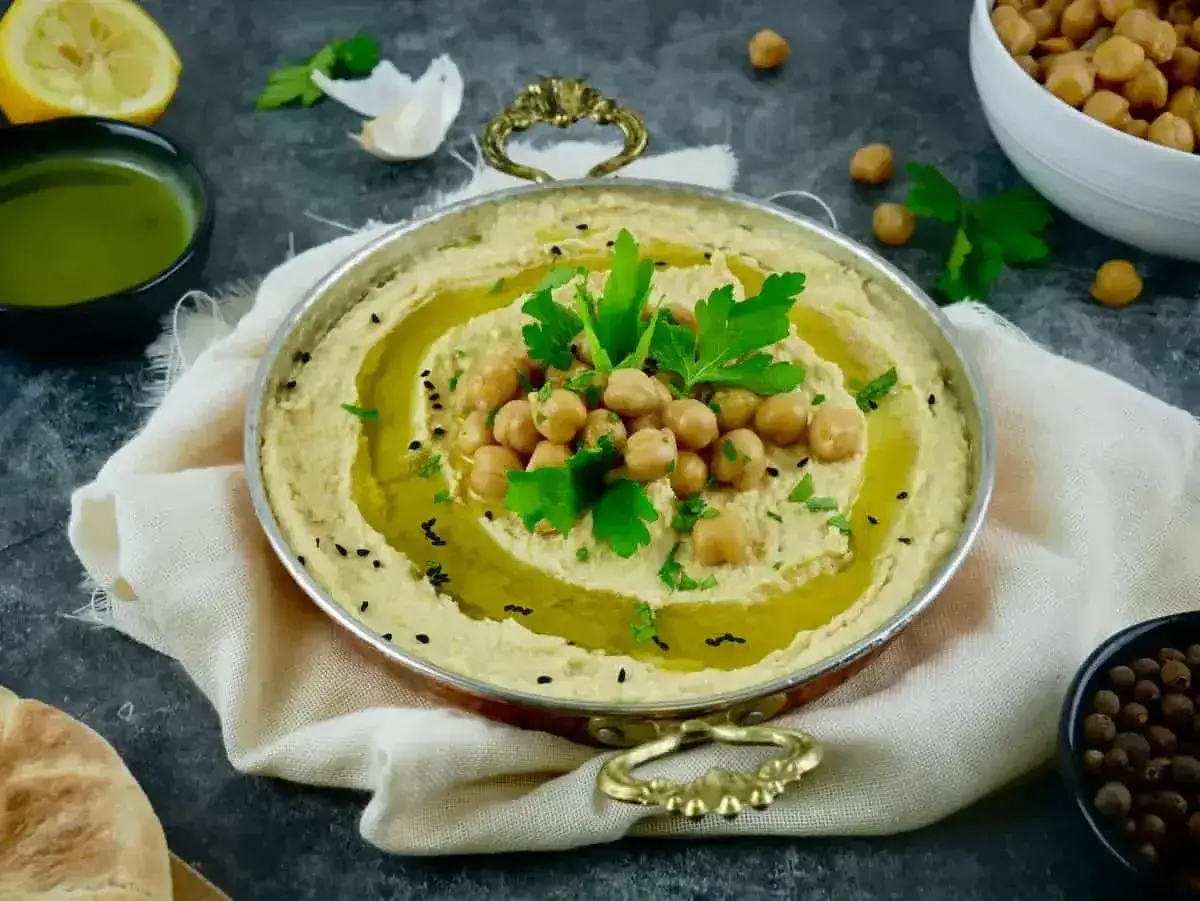 Pyszny, kremowy humus, czyli pasta z ciecierzycy, ozdobiony ziarnami i natką pietruszki. Obok cytryna, czosnek i oliwa.