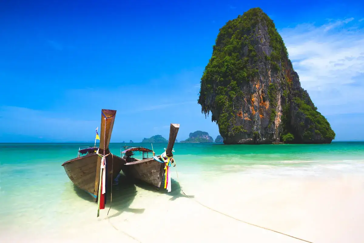 Dwie łodzie czekają na plaży. Czy to Krabi czy Phuket? Turkusowa woda, biały piasek i skalista wyspa tworzą rajski widok.