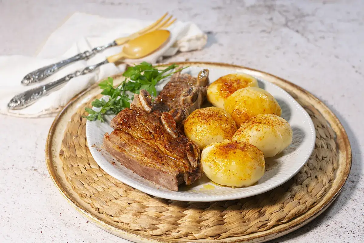 Un plato de carne o caldeiro con patatas cocidas, adornado con perejil fresco.