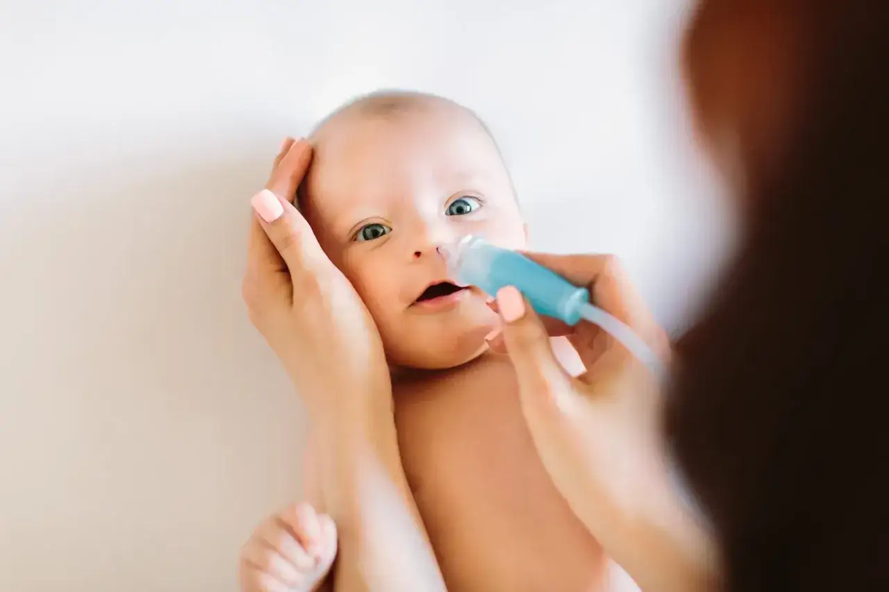 Mama delikatnie oczyszcza nosek niemowlaka z katarem za pomocą aspiratora.