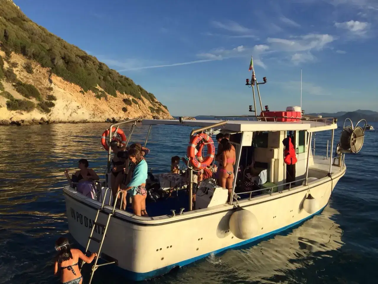 Gente su una barca per pescaturismo, con una collina verdeggiante sullo sfondo.