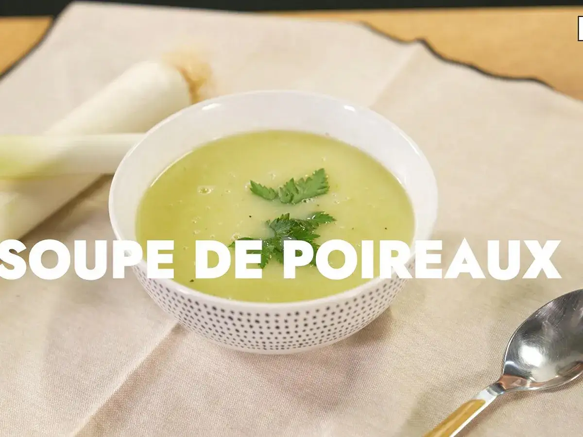 Un bol de soupe de poireaux onctueuse, garnie de persil frais, avec des germes de poireaux en arrière-plan.