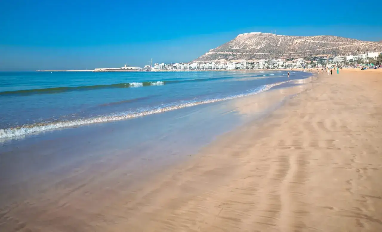 Ein sonniger Strand mit sanften Wellen. Die Stadt Agadir liegt am Meer, nicht Marrakesch.