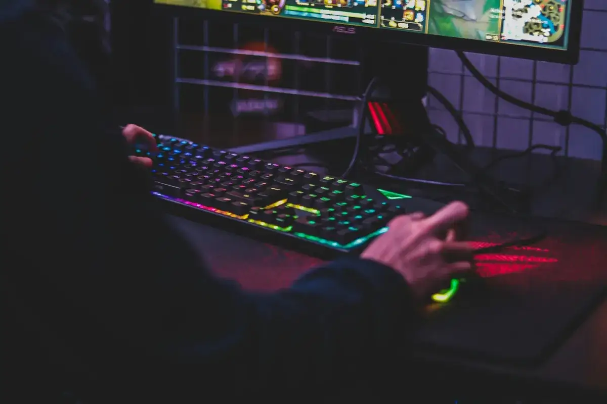 Gracz używa podświetlanej klawiatury i myszy do gry na komputerze, być może przez emulator androida.