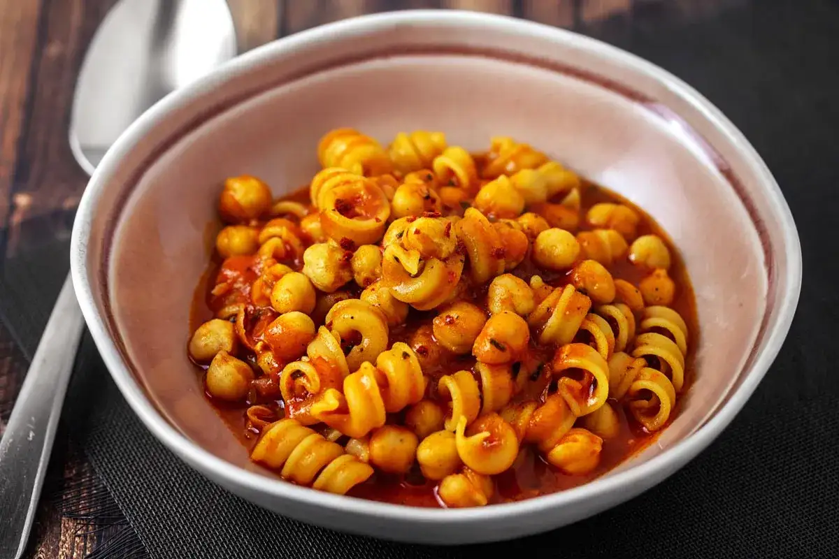 Herzhaftes ceci rezept: Spiralnudeln mit Kichererbsen in Tomatensauce, garniert mit Kräutern und Chili.