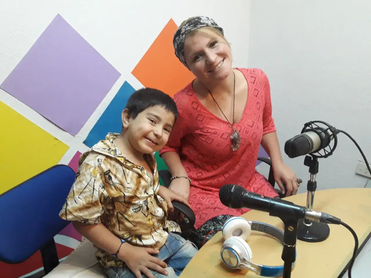 Un niño indigo sonriente, con una mujer, se preparan para grabar un podcast.