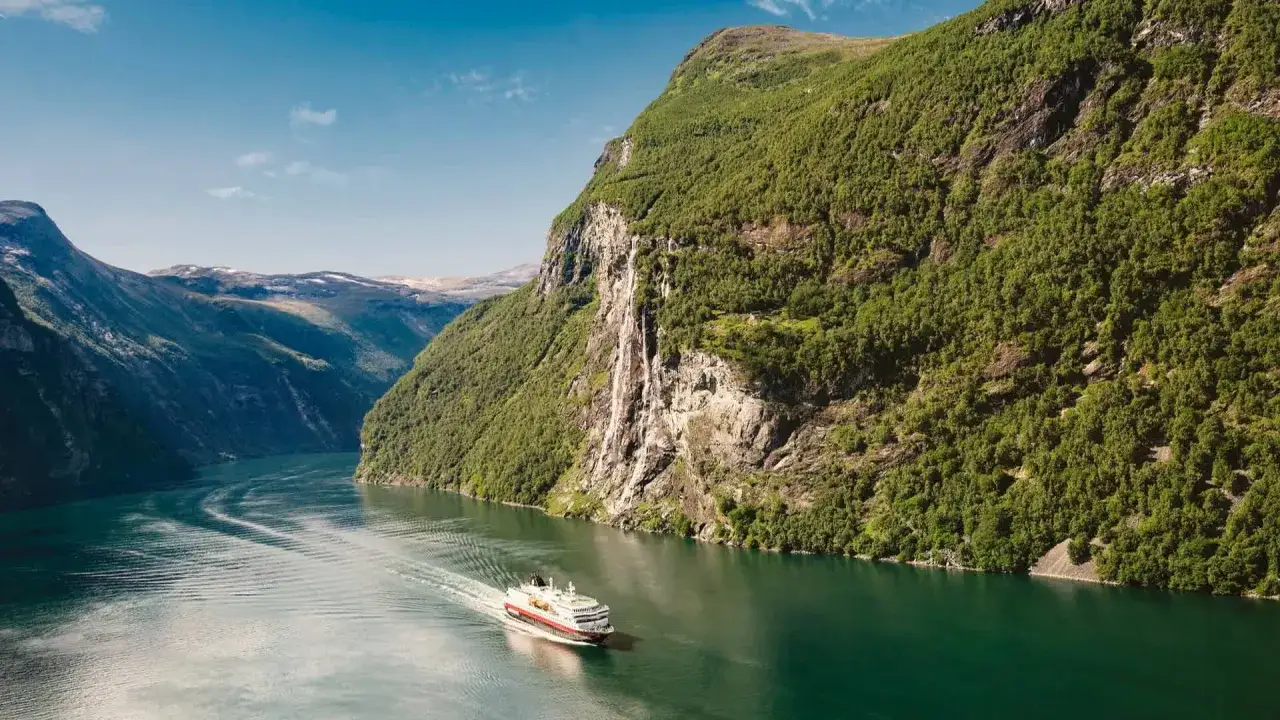 Nave in crociera tra fiordi norvegesi, con cascate e montagne verdi. Il periodo migliore per una crociera fiordi è l'estate.