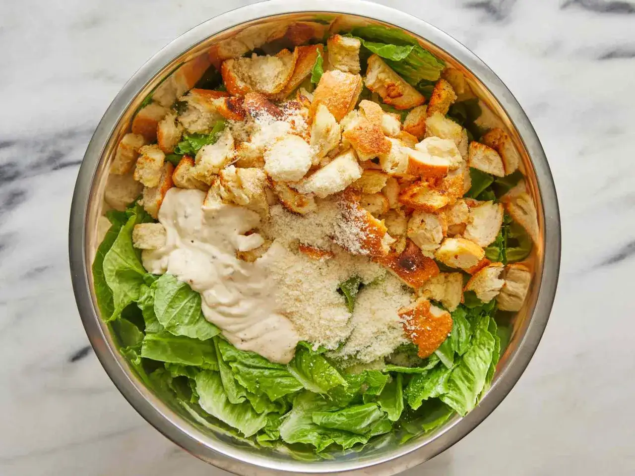 Ensalada César en un bol de metal, con lechuga romana, picatostes crujientes, queso rallado y una cremosa salsa César.