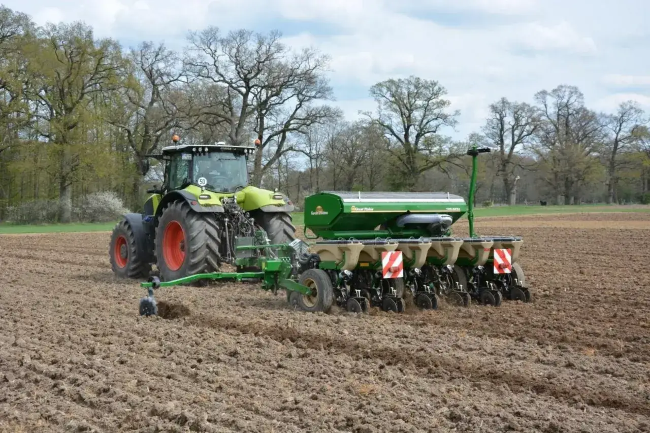 Traktor z siewnikiem pracuje na polu, przygotowując ziemię. To idealny moment, kiedy siać pszenżyto jare, by uzyskać obfite plony.