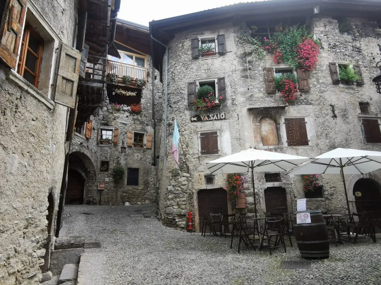 Un vicolo acciottolato nel **canale di Tenno cosa vedere**: case in pietra con fiori, finestre con persiane e tavolini all'aperto.