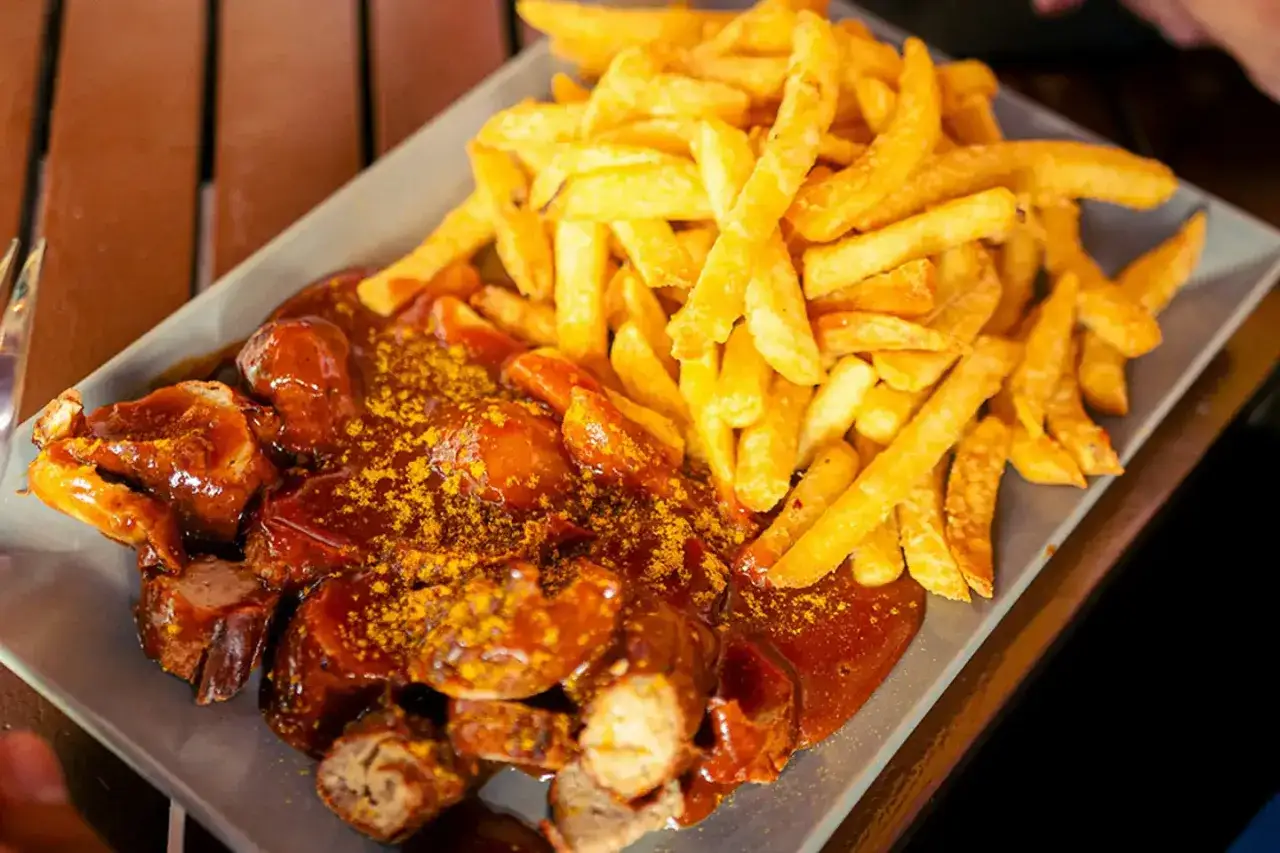 Currywurst z frytkami, klasyka, co zjeść w Berlinie. Pyszne danie na talerzu, idealne na szybki posiłek.