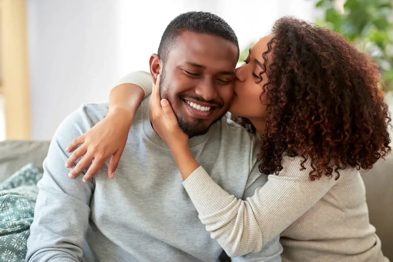 Une femme embrasse tendrement un homme souriant. Un moment de complicité qui aide à savoir si un homme est sincère.