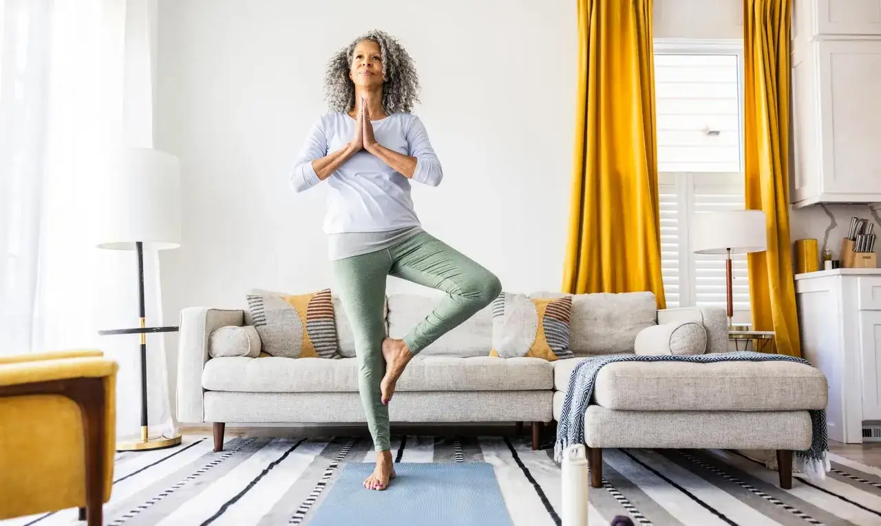 Femme pratiquant le yoga à la maison gratuit, en équilibre sur un tapis bleu.