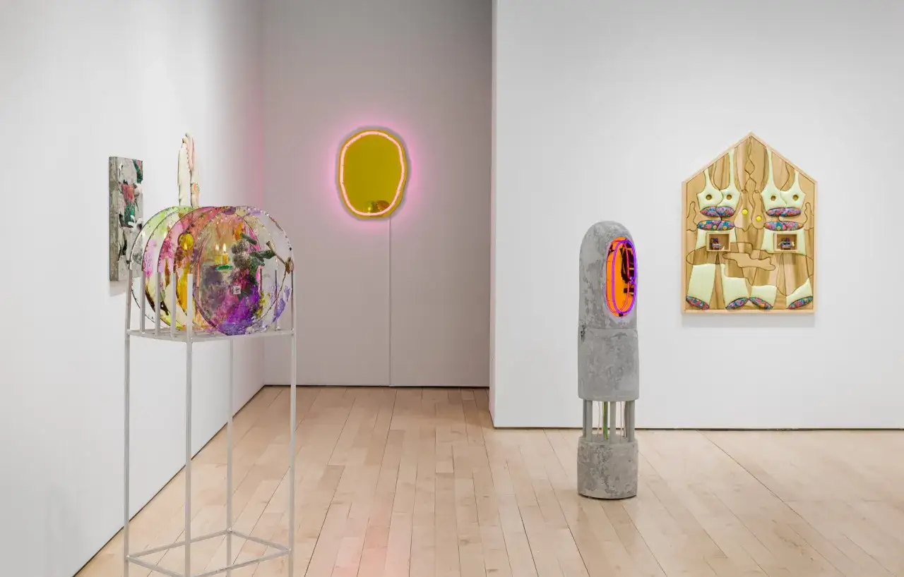 Art installation at Asya Geisberg Gallery featuring colorful sculptures, a neon-lit mirror, and a concrete pillar with neon accents.