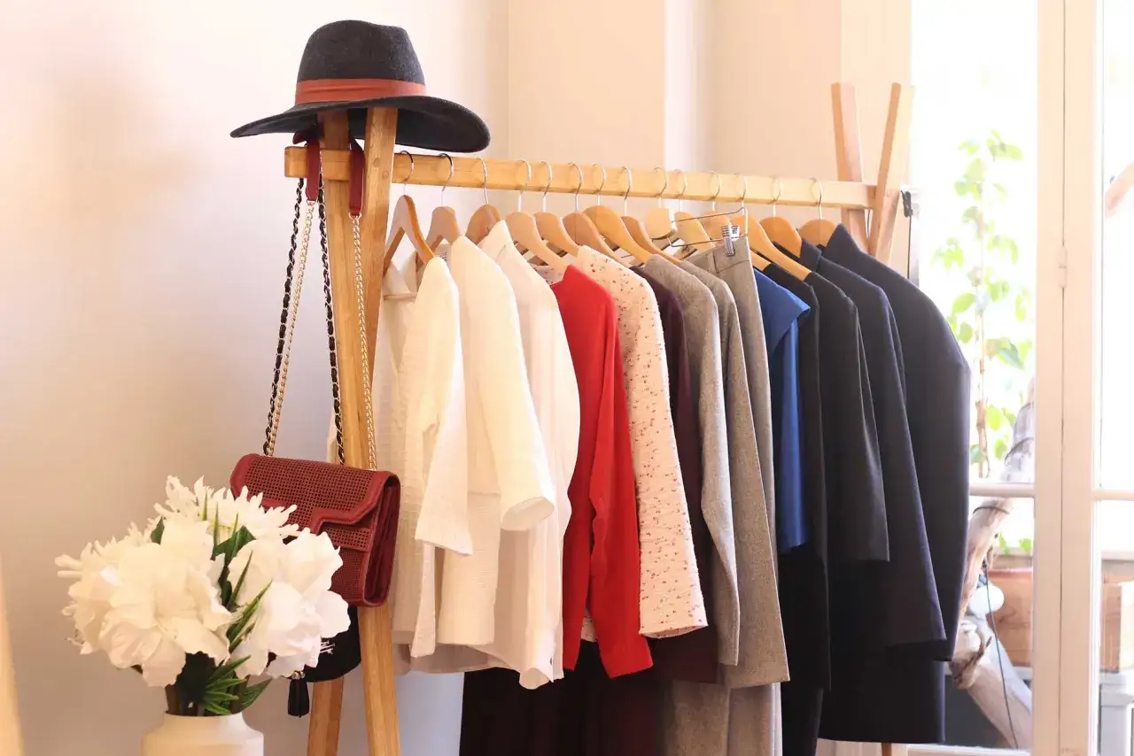 Un portant à vêtements bien organisé, avec un chapeau et des sacs, illustre comment éviter la surconsommation en privilégiant la qualité et la polyvalence.