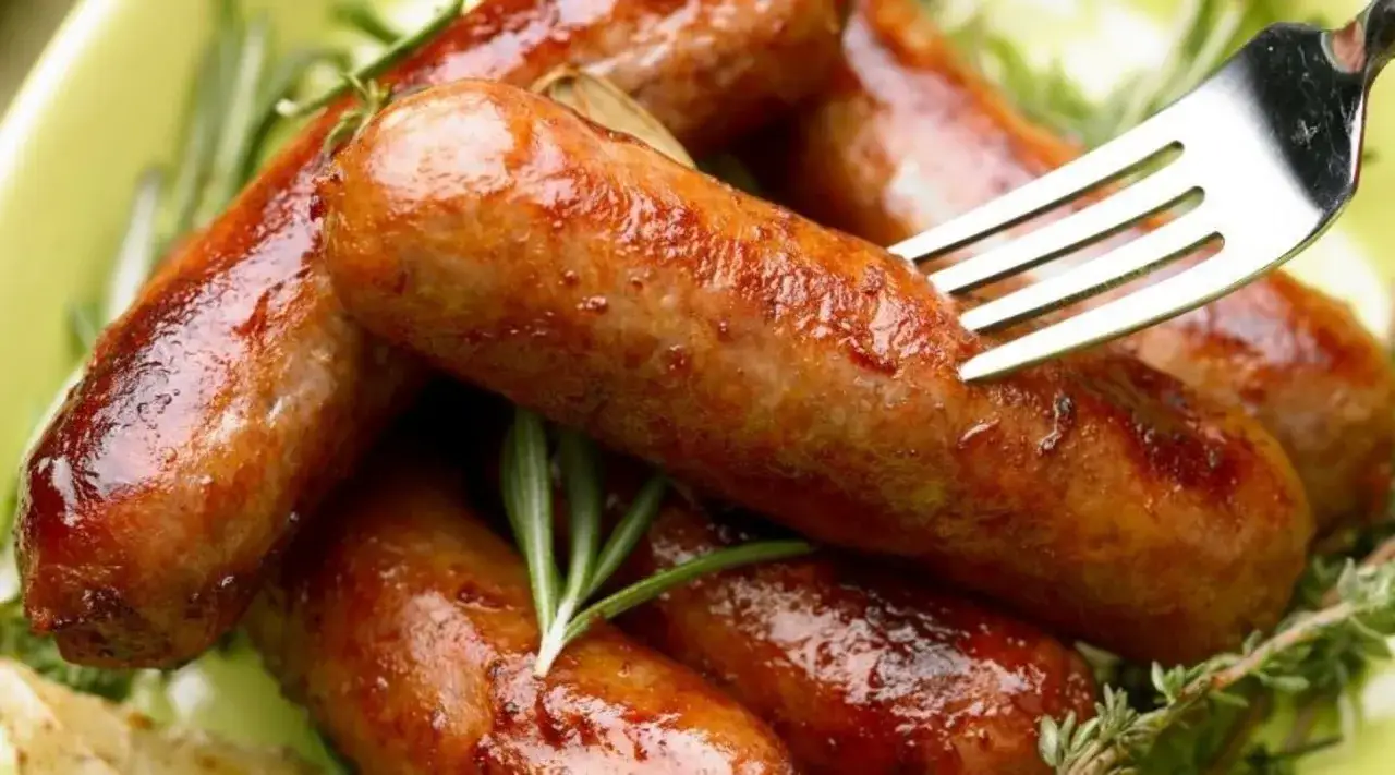 Soczysta kiełbasa z piekarnika, rumiana i aromatyczna, podana z gałązkami rozmarynu. Widok zachęca do spróbowania.