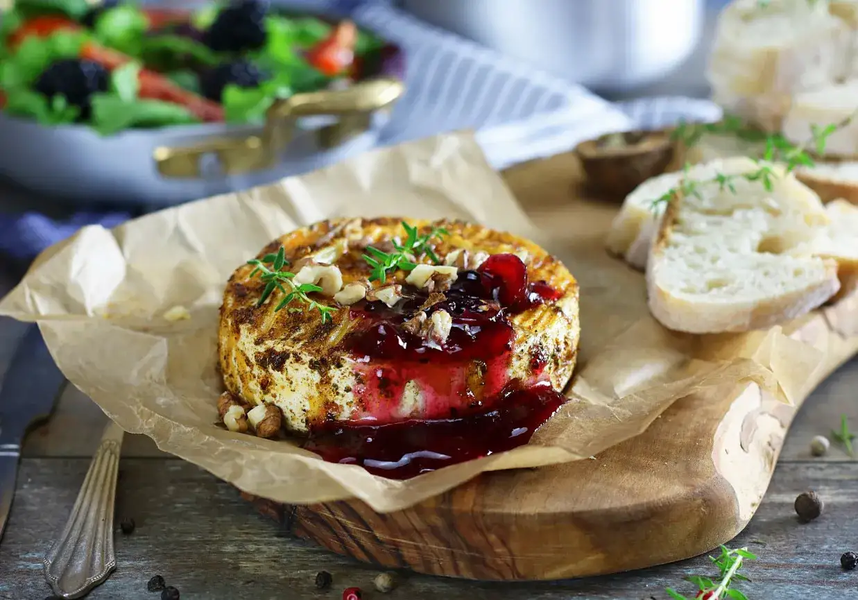 Pyszny camembert z grilla polany konfiturą, posypany orzechami i ziołami, podany z pieczywem.