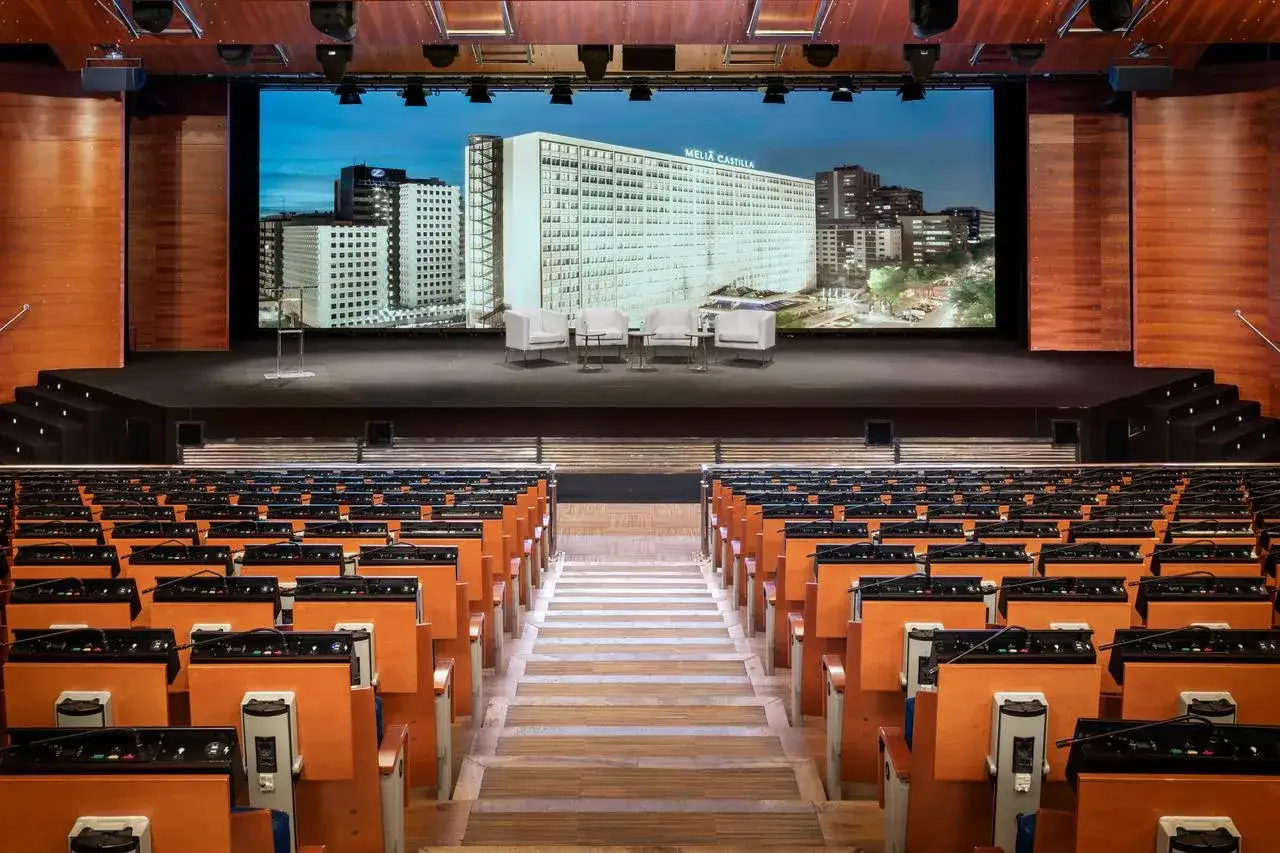 Sala de conferencias lista para un evento de **turismo MICE**. Butacas, escenario con pantalla gigante y mobiliario moderno.